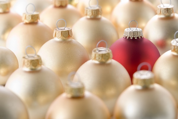 Viele cremegoldene Weihnachtskugeln dicht gereiht, eine einzelne rote Kugel sticht in der Bildmitte hervor