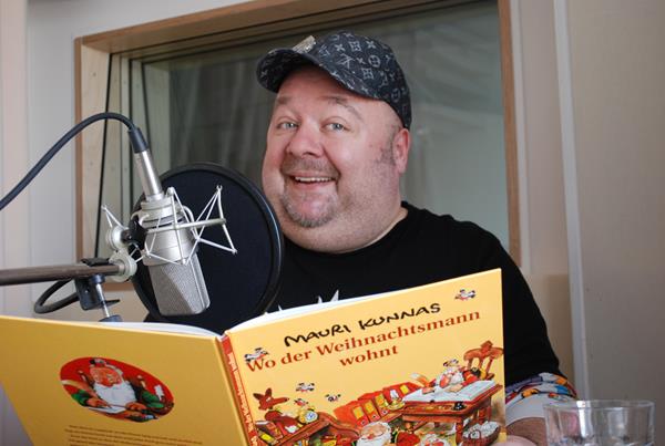 Dirk Bach mit Kappe liest im Tonstudio vor Mikrofon aus Mauri Kunnas Buch Wo der Weihnachtsmann wohnt