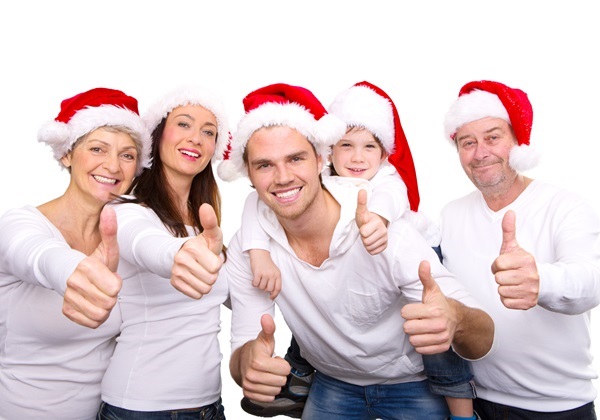 Fünfköpfige Familie in weißen Pullovern und roten Weihnachtsmützen zeigt Daumen hoch