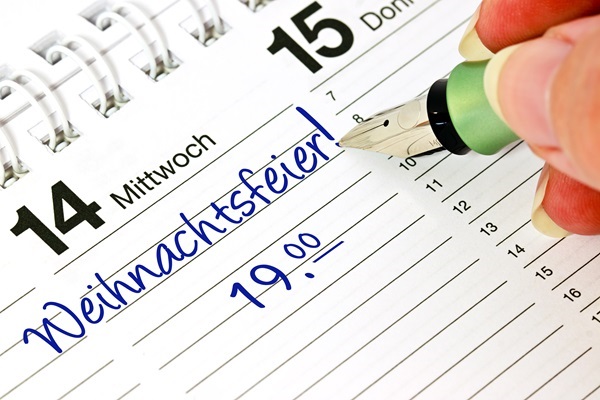 Hand schreibt mit Füllfederhalter Weihnachtsfeier! und 19.00 Uhr in blau auf den 14. Dezember im Tischkalender