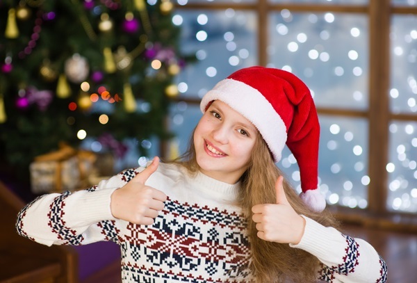 Mädchen mit roter Weihnachtsmütze und Norwegerpullover zeigt mit beiden Händen Daumen hoch