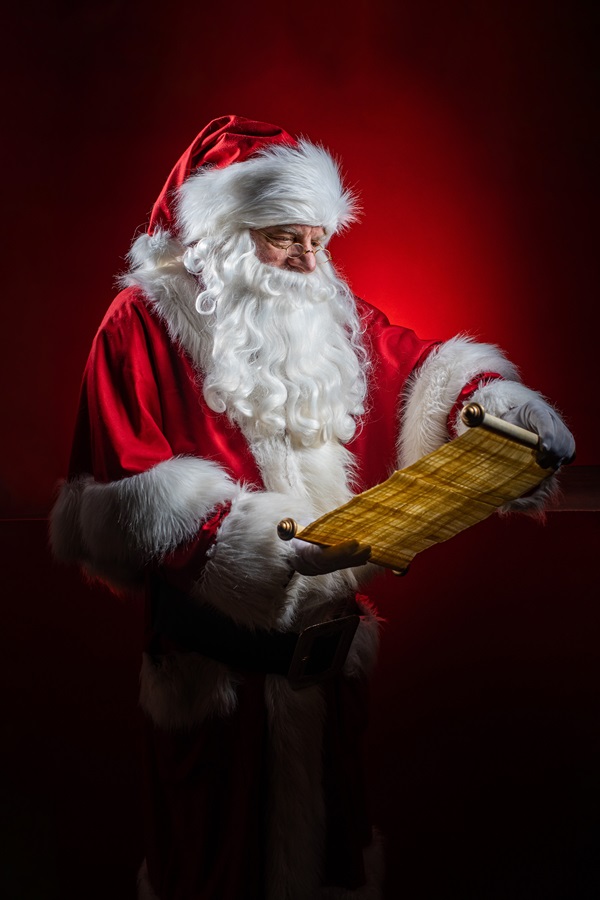 Weihnachtsmann Claudius liest Schriftrolle, roter Mantel, weißer Bart und goldene Brille, roter Hintergrund