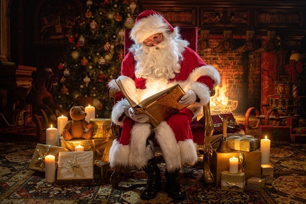 Weihnachtsmann Claudius im Thronsessel mit Goldenem Buch, Kerzen und Geschenken im Kaminzimmer nebst Kerzen