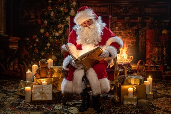 Weihnachtsmann Claudius im Thronsessel mit Goldenem Buch, Kerzen und Geschenken im Kaminzimmer mit Kerzen
