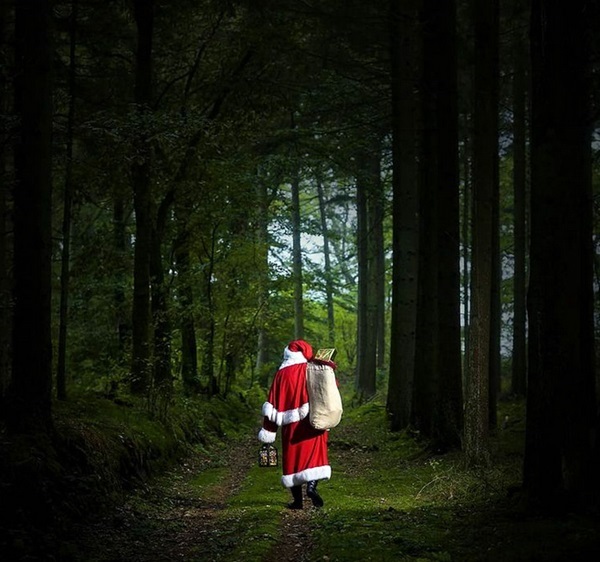 Weihnachtsmann Claudius von hinten auf moosigem Waldweg, Sack auf dem Rücken, Laterne in der Hand, Licht am Wegende