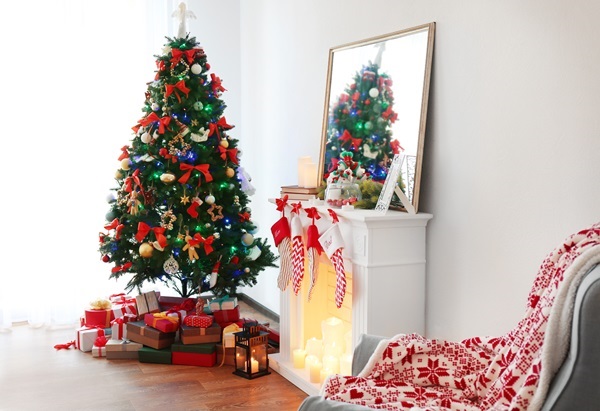 Wohnzimmer mit großem Weihnachtsbaum, weißem Kamin mit Strickstrümpfen, Spiegel und Geschenken darunter